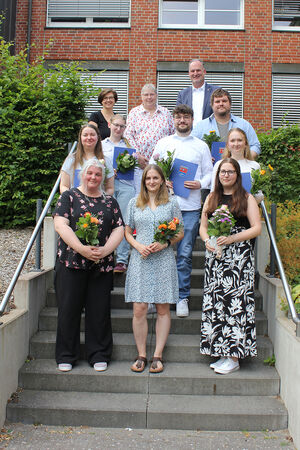 Bild vergr&ouml;&szlig;ern: Auf dem Foto sind die diesjährigen Absolventinnen und Absolventen der Kreisverwaltung Plön zu sehen. Sie stehen mit ihren Urkunden und kleinen Blumensträußen zusammen mit der Gleichstellungsbeauftragten Yvonne Deerberg, der Personalratsvorsitzenden Christel Pfau und Landrat Björn Demmin auf dem Treppenaufgang zum Kreistagssitzungssaal.