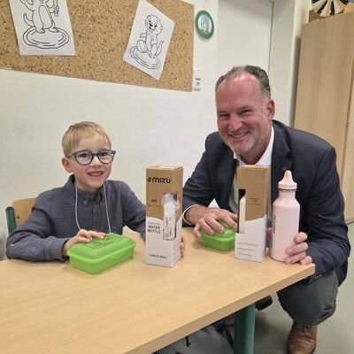 Das Foto zeigt Landrat Björn Demmin bei der Übergabe der Brotdosen und der Trinkflaschen zusammen mit dem Schüler Luan Kock. 
